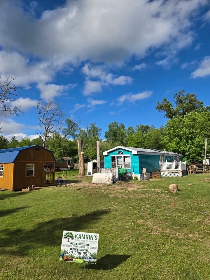 Tiny home display lot with turquoise and brown portable structures on green grass, blue sky with clouds, and Kamrin's business sign