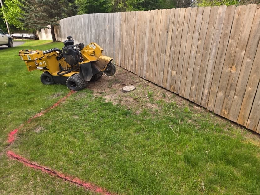 Yellow and black riding lawn mower with attached equipment on residential lawn with wooden fence and red survey marks